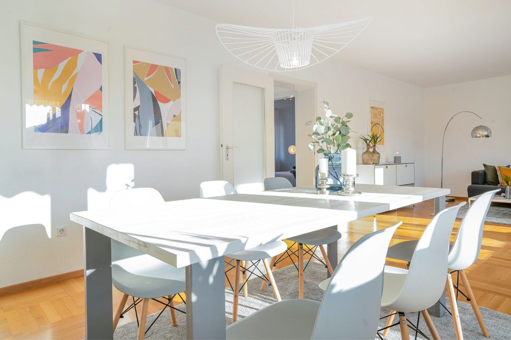 Heike Uhlemann – Deine Home Staging Expertin. Auf dem Foto ist ein Wohnzimmer zu sehen, dass von natürlichem Tageslicht durchflutet wird und auf dem Tisch eine frühlingshafte Blumendekoration hat.
